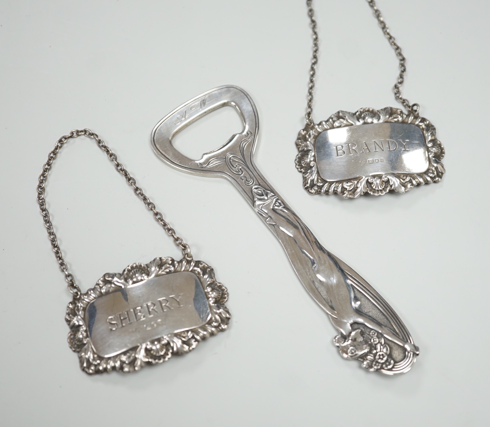 A pair of Queen Elizabeth II silver wine labels, 'Sherry & Brandy', A. Chick & Sons, Ltd, London, 1975 and an Art Nouveau style silver plated bottle opener.